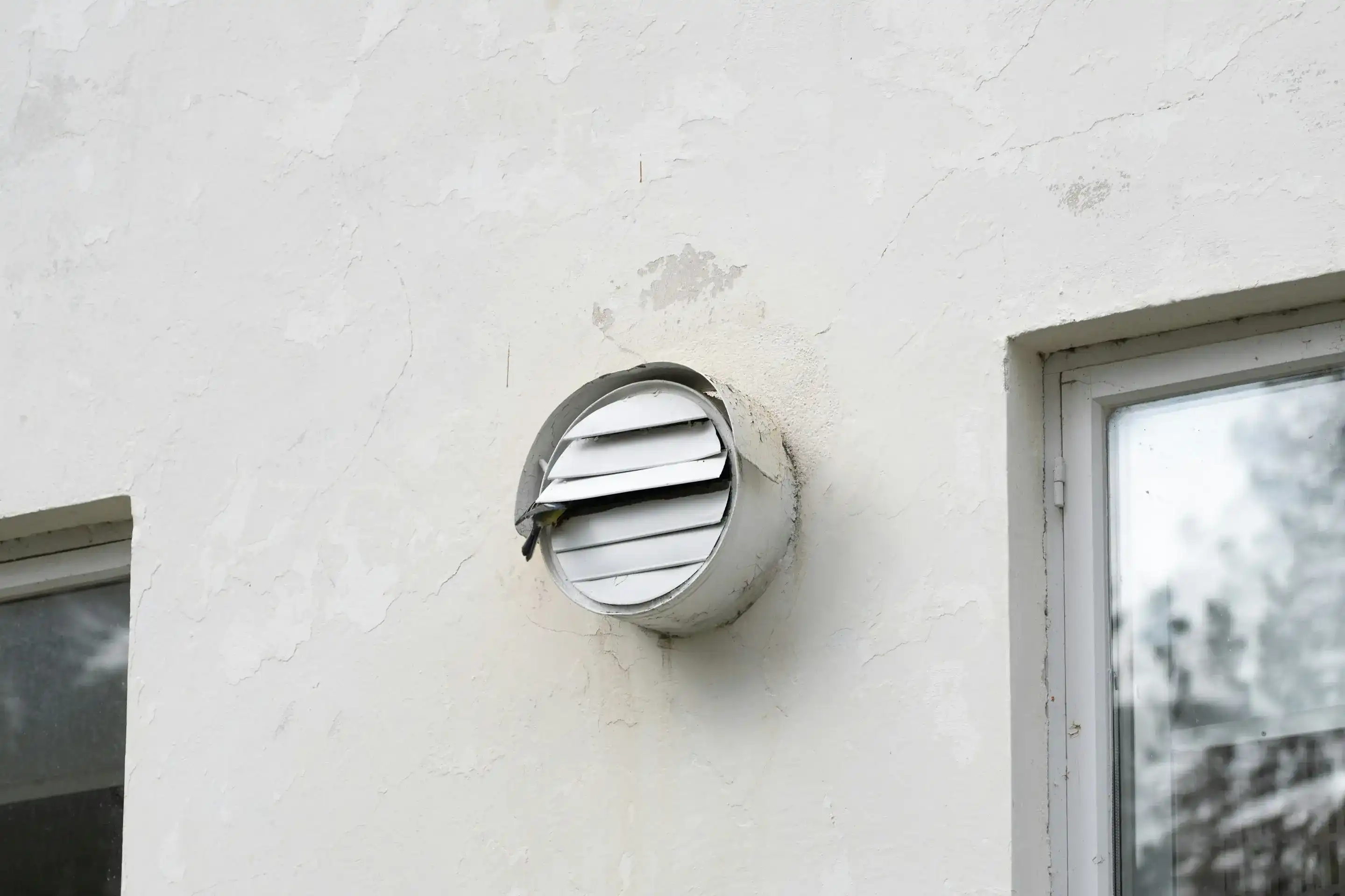 Round dryer vent cap mounted on a white stucco exterior wall