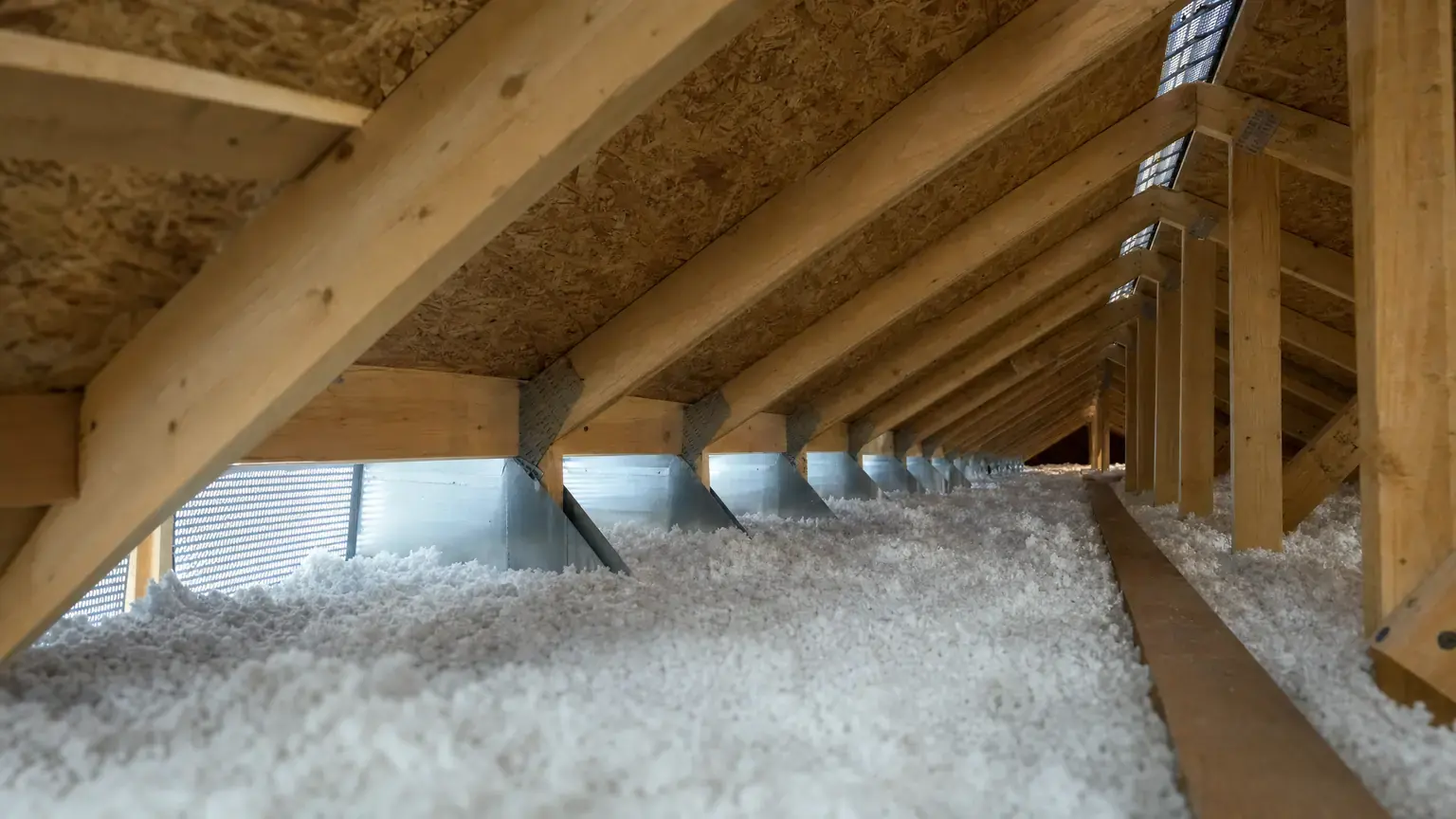 Attic ventilation path from open soffit vents at the eave, past baffles holding insulation clear, to a continuous ridge vent overhead