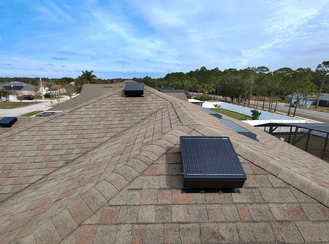Solar attic fan mounted near the ridge of a shingled Brevard County roof, with a second unit further along the same ridge
