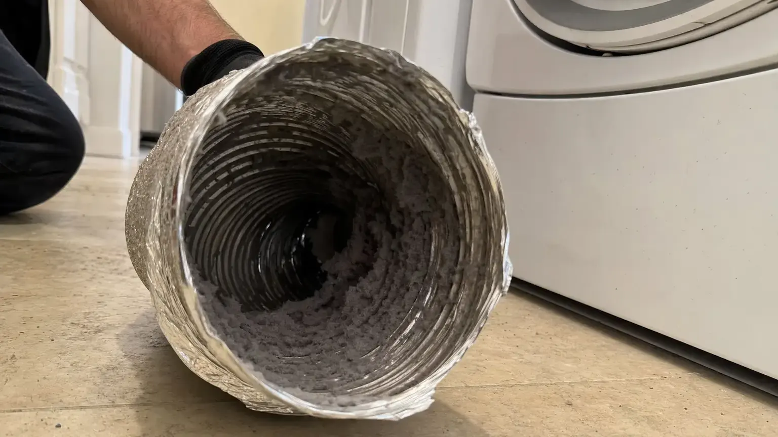 Flexible dryer duct opened to show heavy matted lint packed along its ribbed inner wall