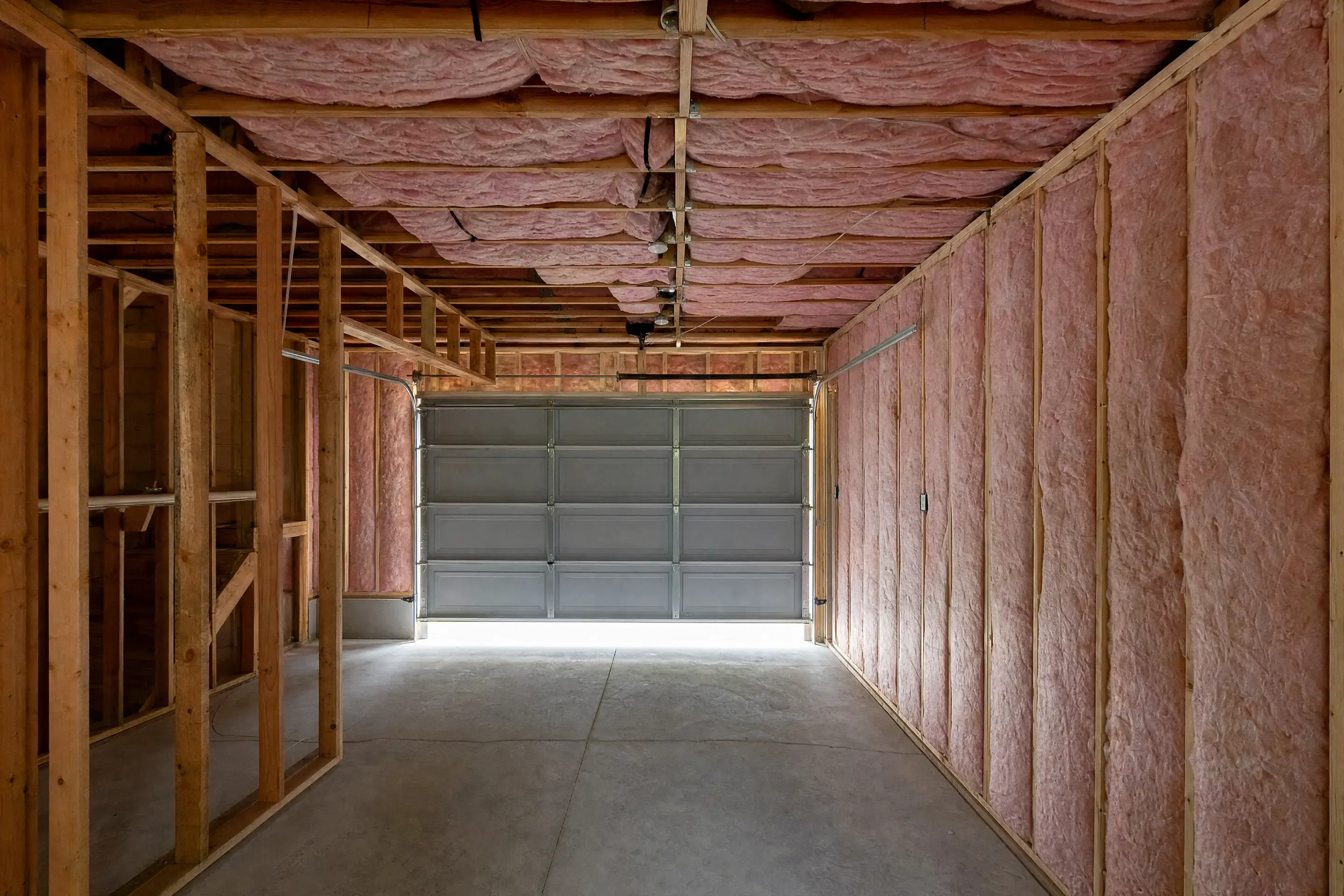 Fiberglass batt insulation fitted between wall studs and ceiling joists in a garage