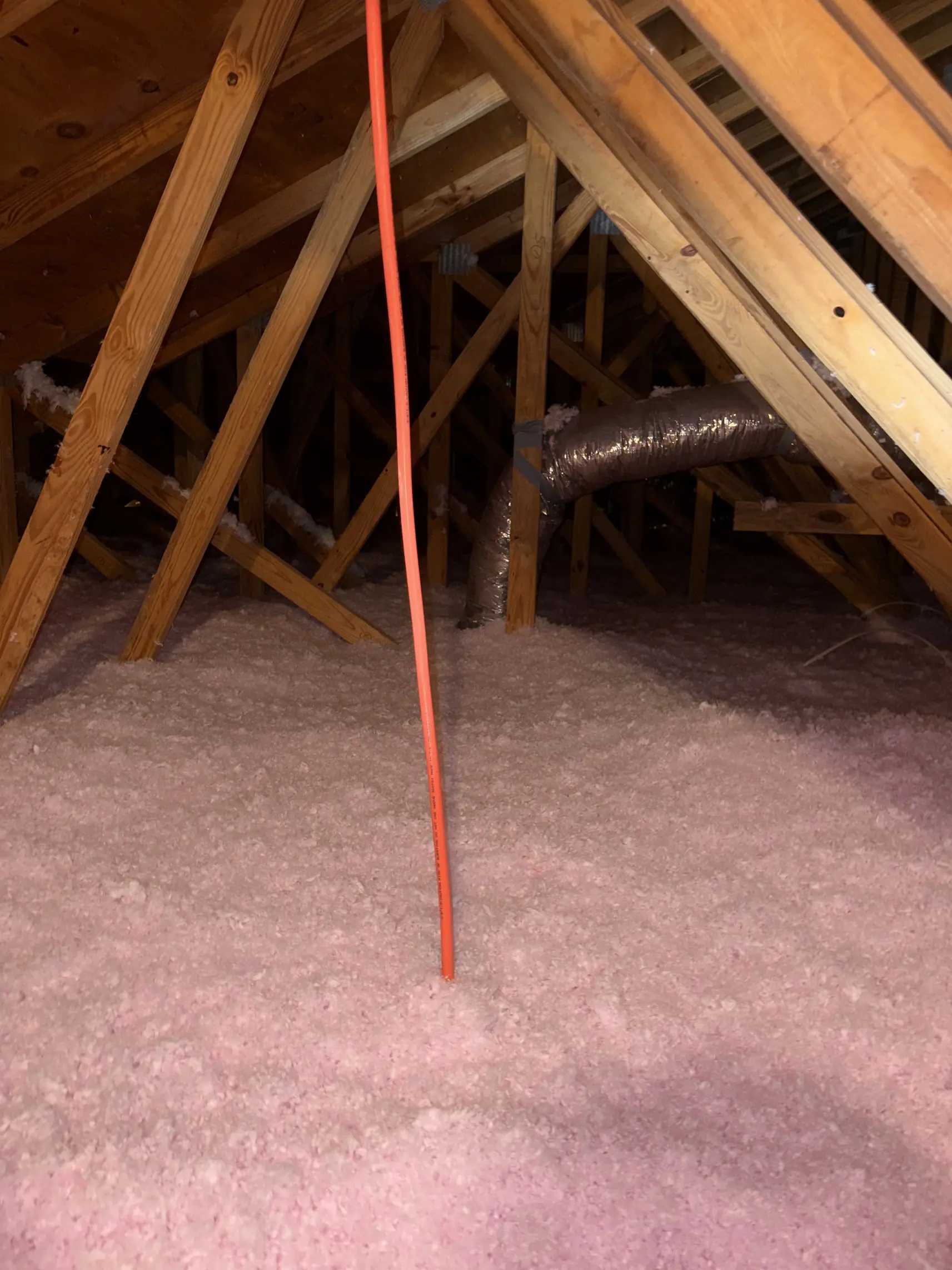 Blown-in fiberglass insulation laid to an even depth across an attic floor between wood trusses