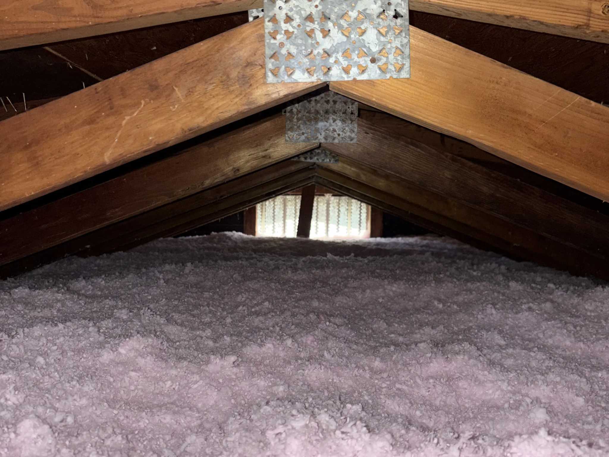 Pink blown-in fiberglass insulation laid level under the roof ridge of a Brevard County attic, gable vent at the far end