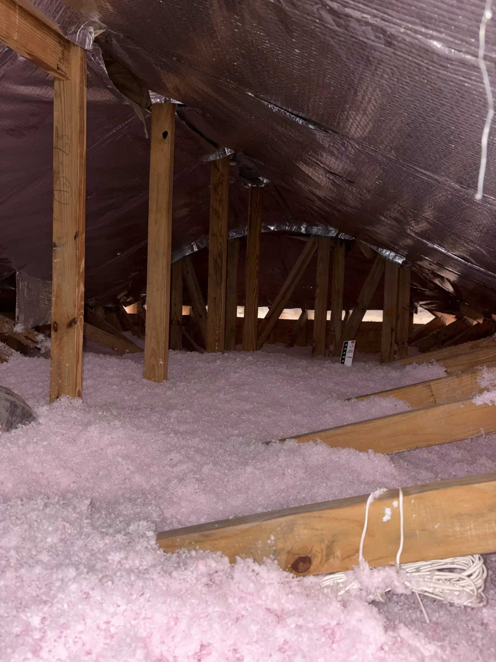 Blown-in fiberglass insulation filling the truss bays of an attic with a foil radiant barrier already fitted under the roof deck