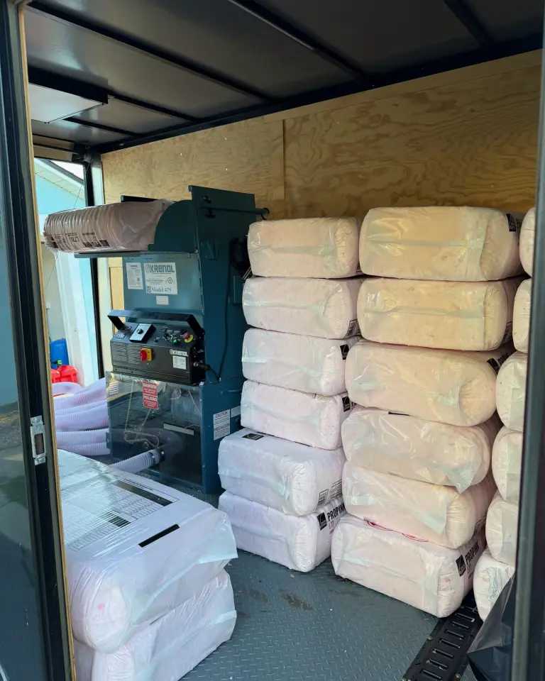 The blowing machine and stacked bags of pink fiberglass insulation loaded for a job