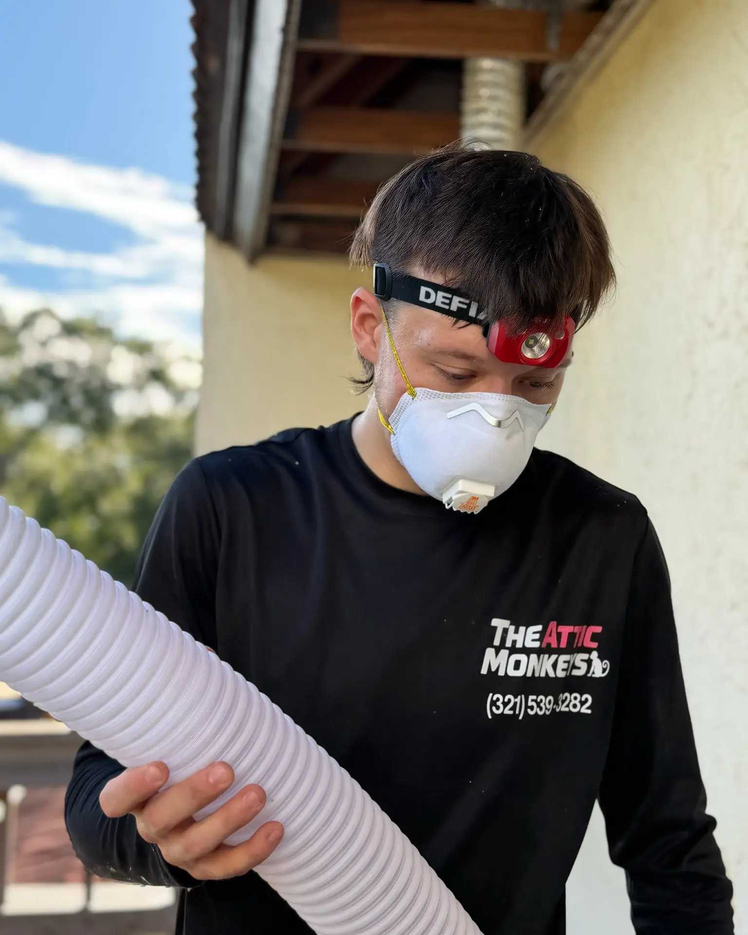 Matt Bunker in a respirator and headlamp, handling the insulation blowing hose on a job