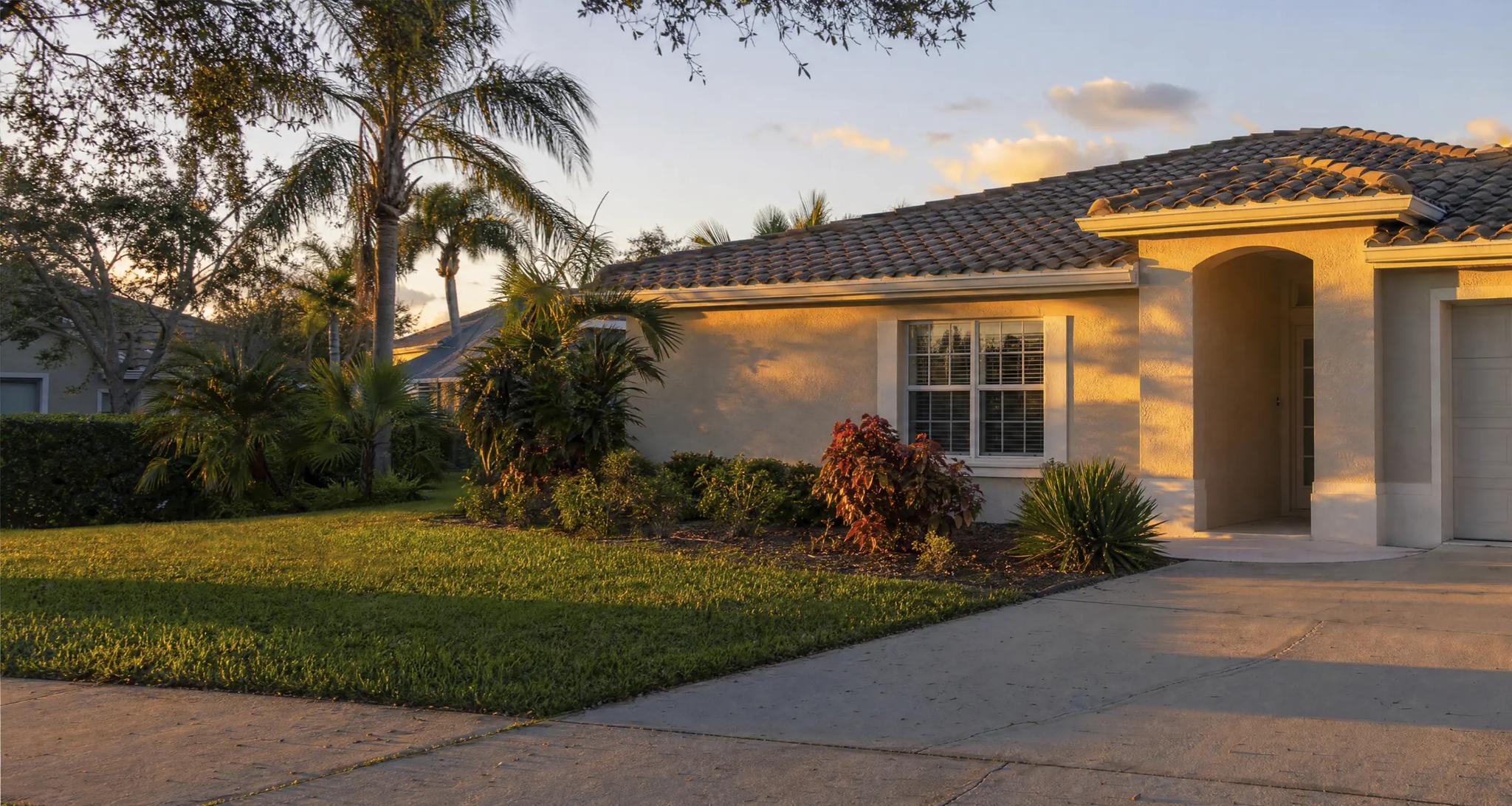 Single-story stucco house with a tile roof and palms in the yard, lit by low evening sun